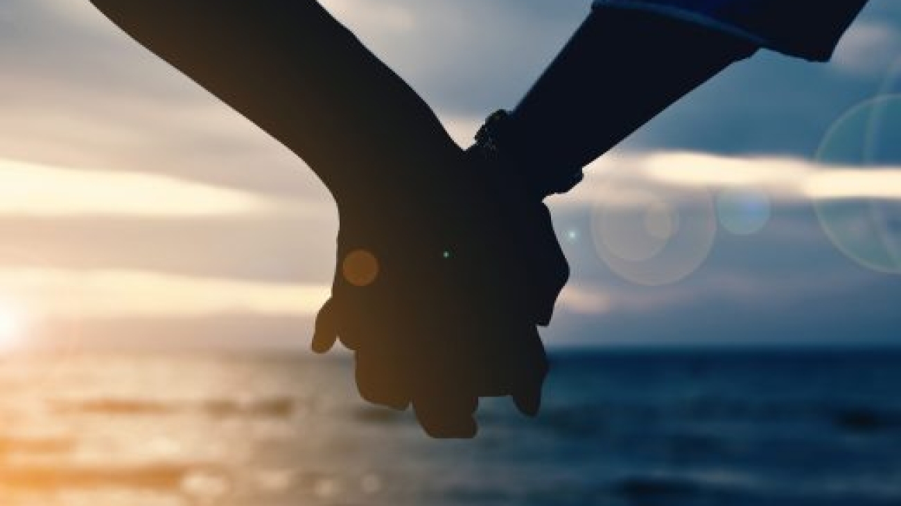 Cropped Hands Of Couple At Beach Against Cloudy Sky During Sunset