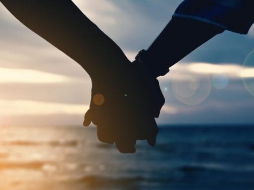 Cropped Hands Of Couple At Beach Against Cloudy Sky During Sunset