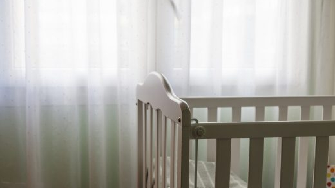 a baby white craddle corner with dim relaxing light from a window with curtains. Concept of motherhood and having a baby at home with copy space.