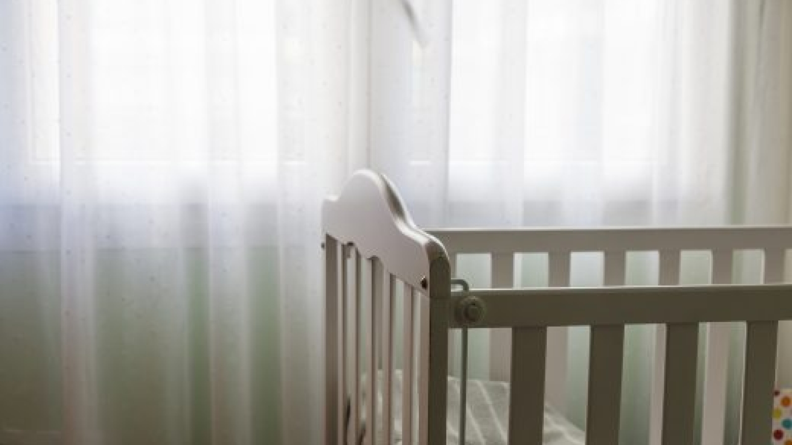 a baby white craddle corner with dim relaxing light from a window with curtains. Concept of motherhood and having a baby at home with copy space.