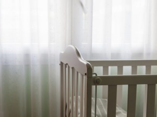 a baby white craddle corner with dim relaxing light from a window with curtains. Concept of motherhood and having a baby at home with copy space.