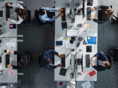 Top Down View of Diverse Colleagues Working In Corporate Office of Hedge Fund. Using Desktop Computers, Discussing Documents, Analyzing Data. Concept of Teamwork and Professional Business Environment