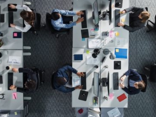 Top Down View of Diverse Colleagues Working In Corporate Office of Hedge Fund. Using Desktop Computers, Discussing Documents, Analyzing Data. Concept of Teamwork and Professional Business Environment