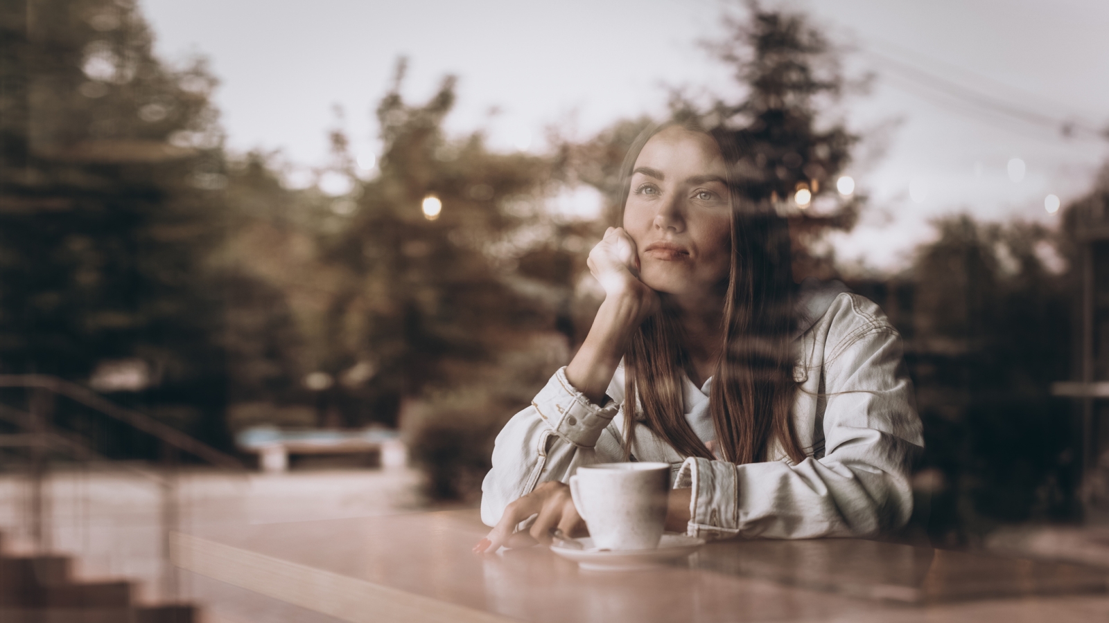 Thoughtful concept. Woman with cap of coffee at a cafe through the window glass.