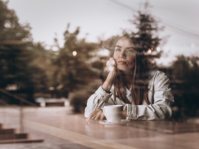 Thoughtful concept. Woman with cap of coffee at a cafe through the window glass.